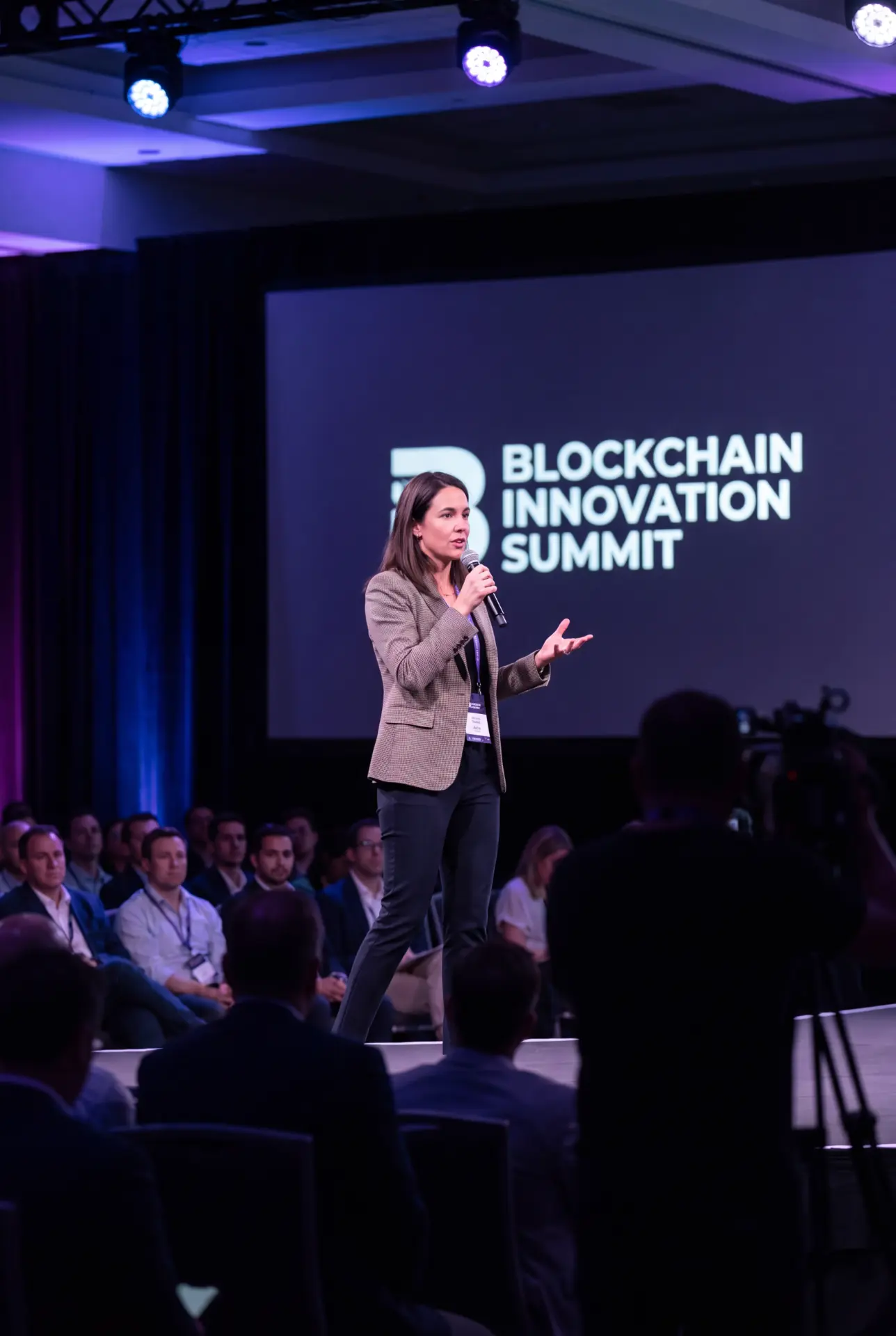 Speaker on stage with a microphone in front of a Blockchain Innovation Summit screen